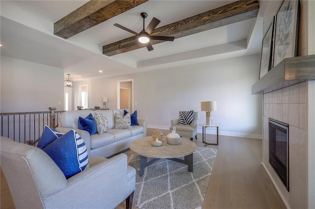 living area with baseboards, beam ceiling, a fireplace, wood finished floors, and a ceiling fan