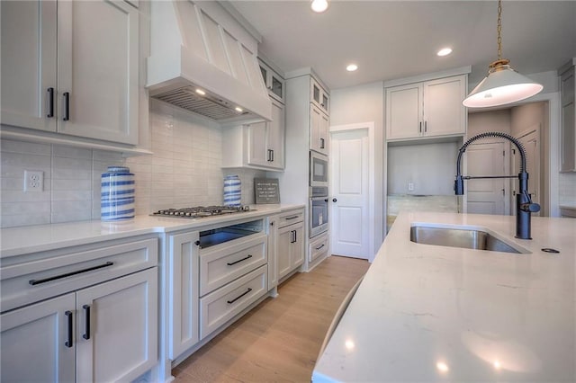 kitchen featuring custom range hood, light stone counters, appliances with stainless steel finishes, light wood-style floors, and a sink