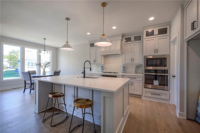 kitchen with a sink, light countertops, light wood-style floors, appliances with stainless steel finishes, and tasteful backsplash