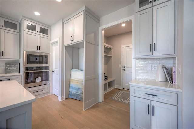 kitchen with light wood finished floors, backsplash, appliances with stainless steel finishes, light countertops, and glass insert cabinets