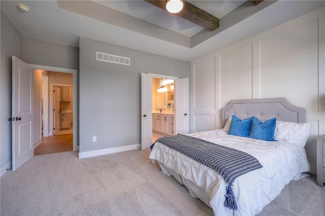 bedroom with visible vents, baseboards, ensuite bath, beamed ceiling, and light colored carpet