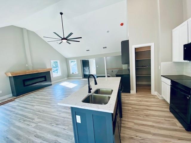 kitchen with high vaulted ceiling, a sink, light wood-style flooring, and stove