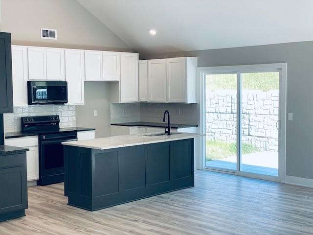 kitchen with a sink, visible vents, white cabinetry, black appliances, and light wood finished floors