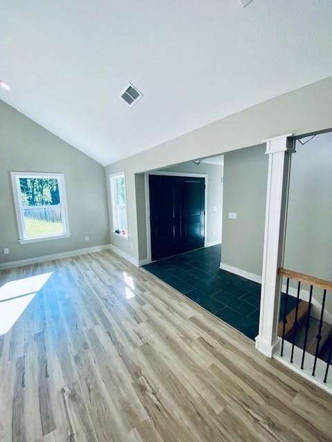 unfurnished living room with lofted ceiling, visible vents, baseboards, and wood finished floors