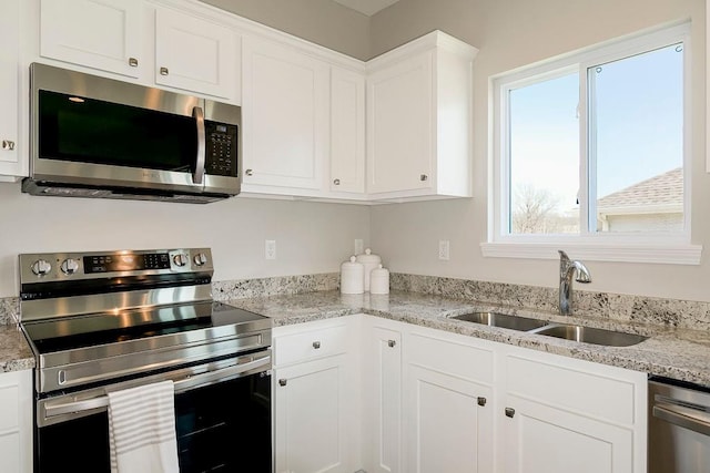 kitchen with white cabinets, stainless steel appliances, light stone counters, and sink