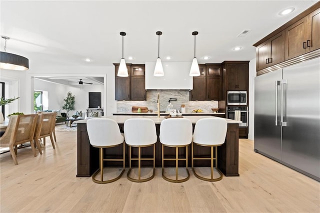 kitchen featuring light hardwood / wood-style floors, hanging light fixtures, a center island with sink, and built in appliances