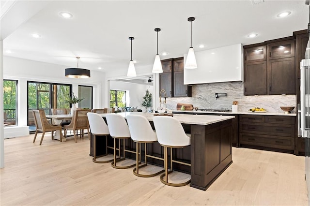 kitchen with dark brown cabinetry, an island with sink, hanging light fixtures, and light hardwood / wood-style floors