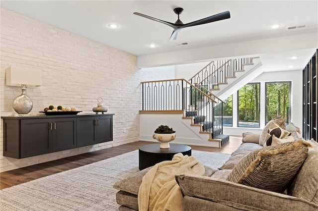 living room featuring dark hardwood / wood-style flooring, ceiling fan, and brick wall