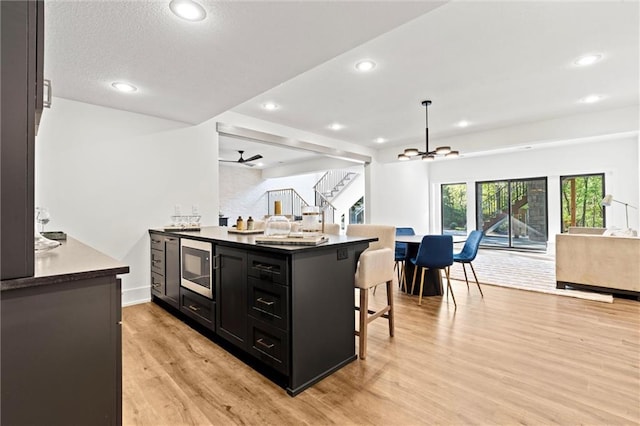 kitchen featuring light hardwood / wood-style floors, a breakfast bar, ceiling fan with notable chandelier, stainless steel microwave, and kitchen peninsula