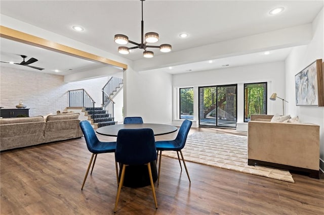 dining room with ceiling fan with notable chandelier, brick wall, and hardwood / wood-style flooring