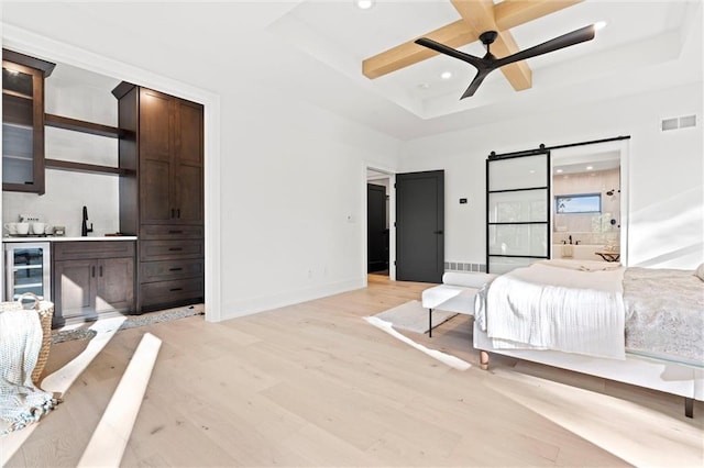 bedroom featuring coffered ceiling, a barn door, light hardwood / wood-style flooring, ceiling fan, and ensuite bath