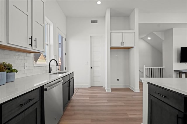 kitchen with decorative backsplash, white cabinets, stainless steel dishwasher, light hardwood / wood-style floors, and sink