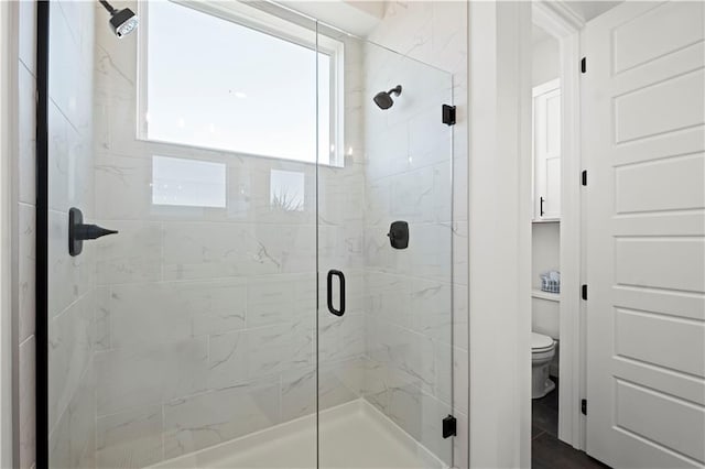 bathroom featuring a shower with door and toilet