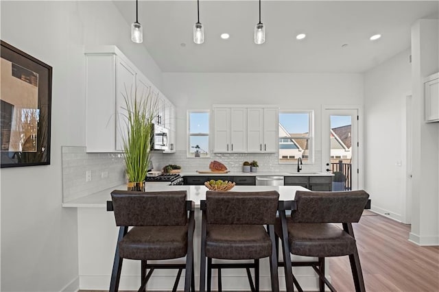 kitchen featuring backsplash, sink, decorative light fixtures, light wood-type flooring, and white cabinets