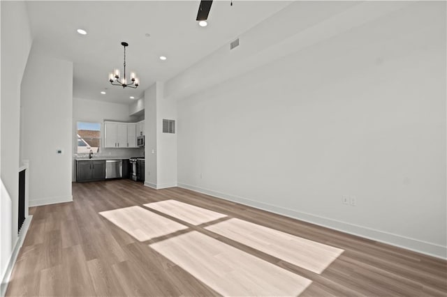 unfurnished living room featuring light hardwood / wood-style flooring, sink, and ceiling fan with notable chandelier