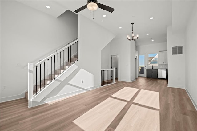 unfurnished living room featuring hardwood / wood-style flooring, sink, and ceiling fan with notable chandelier