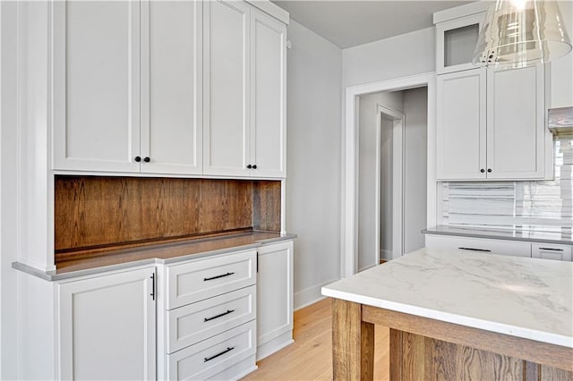 kitchen with light stone countertops, light wood-type flooring, tasteful backsplash, decorative light fixtures, and white cabinetry