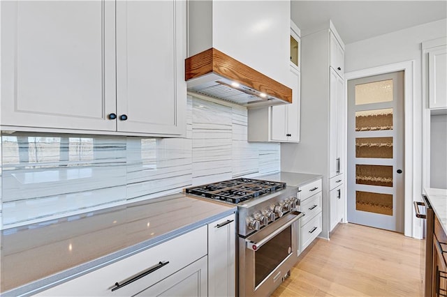 kitchen with light wood-type flooring, light stone counters, custom range hood, stainless steel stove, and white cabinetry