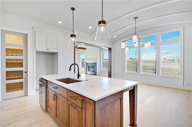 kitchen with sink, an island with sink, hanging light fixtures, and light hardwood / wood-style floors