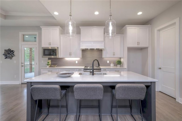 kitchen featuring stainless steel microwave, light wood-type flooring, and a kitchen island with sink