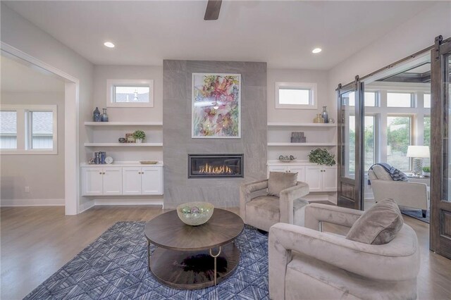 12200 W 138th Pl, Overland Park, KS 66221 - living room featuring a barn door, wood finished floors, a tiled fireplace, baseboards, and built in shelves