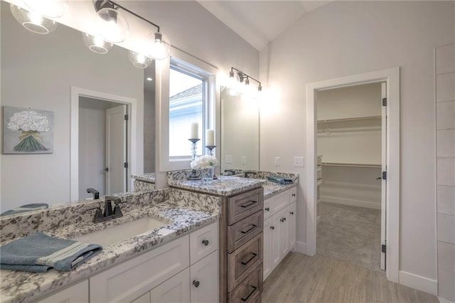 13812 Quigley St, Overland Park, KS 66221 - bathroom featuring wood finished floors, two vanities, vaulted ceiling, a spacious closet, and baseboards
