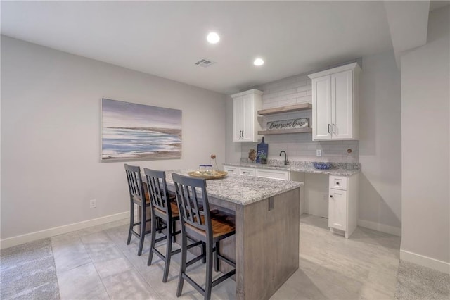 13812 Quigley St, Overland Park, KS 66221 - kitchen featuring white cabinets, light stone counters, decorative backsplash, a kitchen breakfast bar, and a sink
