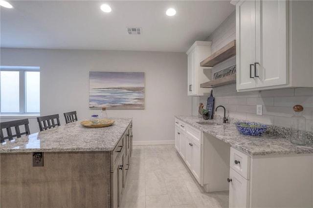13812 Quigley St, Overland Park, KS 66221 - kitchen featuring a sink, baseboards, backsplash, white cabinets, and a center island
