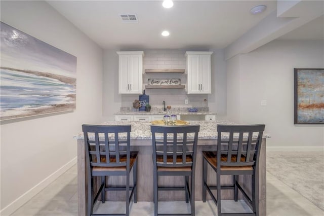 13812 Quigley St, Overland Park, KS 66221 - kitchen featuring white cabinetry, light stone countertops, a sink, a kitchen island with sink, and a breakfast bar