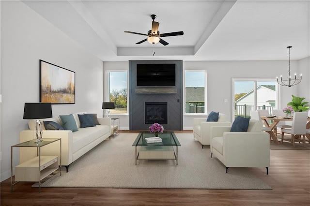 living area with ceiling fan with notable chandelier, a tray ceiling, a fireplace, and wood finished floors