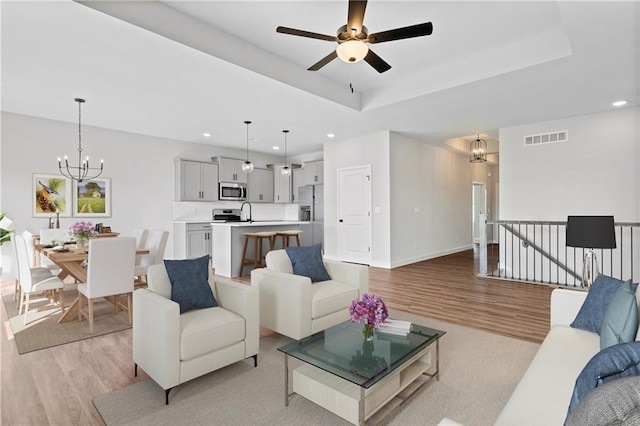 living area featuring a tray ceiling, light wood-style flooring, visible vents, and recessed lighting