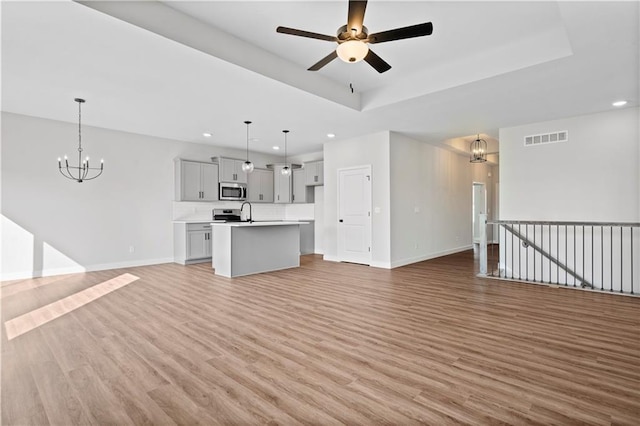 unfurnished living room with light wood finished floors, baseboards, visible vents, and a raised ceiling