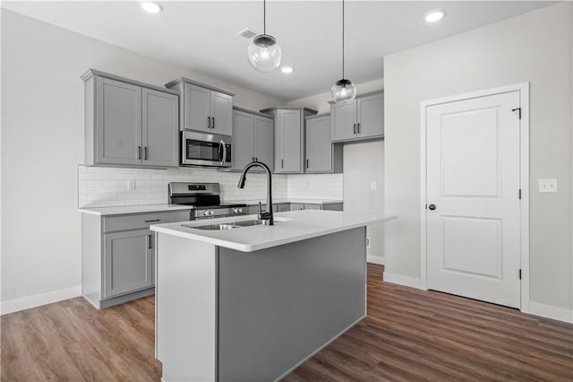 kitchen with stainless steel appliances, a sink, light countertops, a center island with sink, and pendant lighting