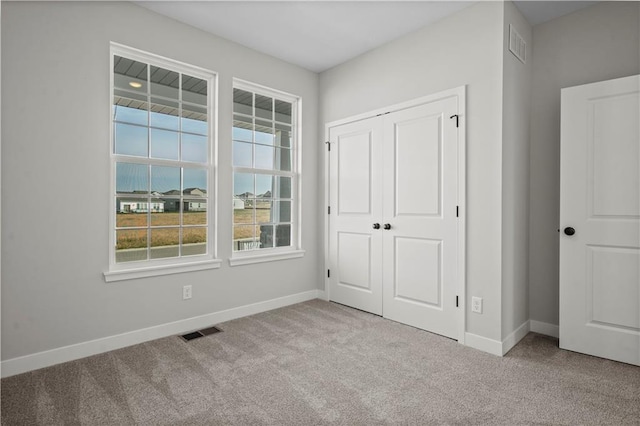 unfurnished bedroom featuring baseboards, a closet, visible vents, and light colored carpet