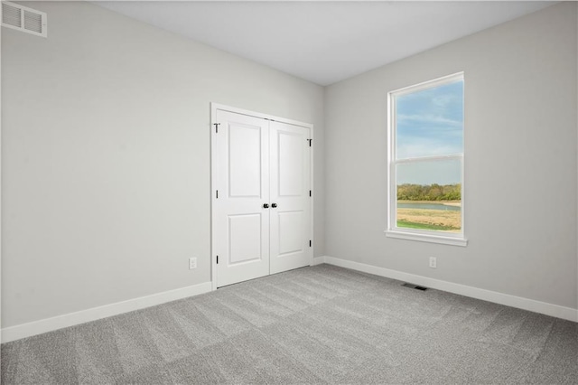 unfurnished bedroom with light colored carpet, a closet, visible vents, and baseboards