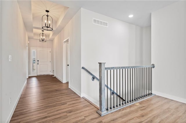 hallway featuring visible vents, an upstairs landing, wood finished floors, a chandelier, and baseboards