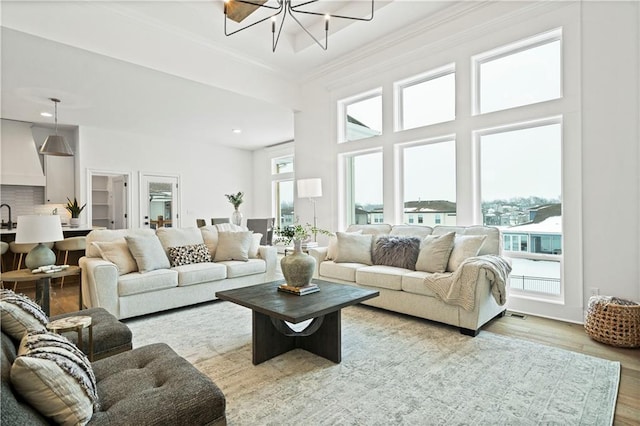 living room with a chandelier, ornamental molding, light wood-type flooring, and sink