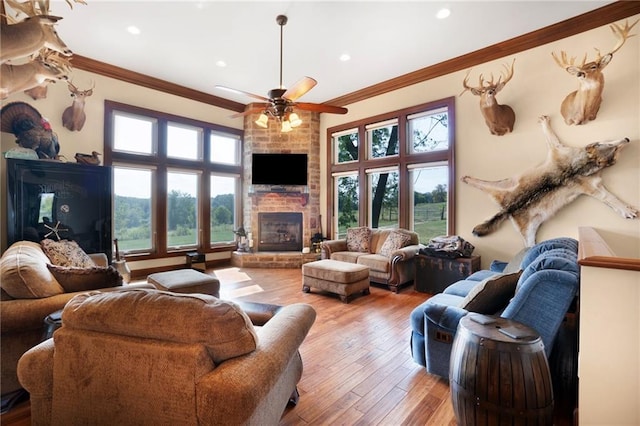 living room featuring a fireplace, brick wall, ceiling fan, crown molding, and light wood-type flooring