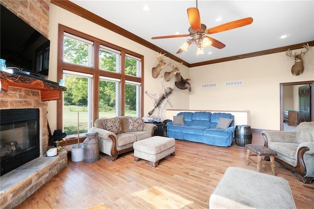 living room with ornamental molding, a stone fireplace, ceiling fan, and light wood-type flooring