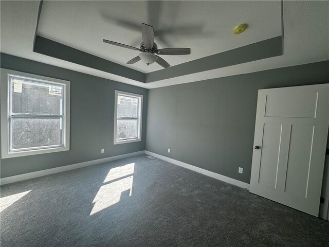 empty room with ceiling fan, dark carpet, and a tray ceiling