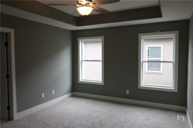 carpeted spare room with a tray ceiling and ceiling fan