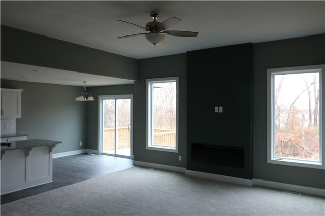 unfurnished living room featuring carpet and ceiling fan with notable chandelier