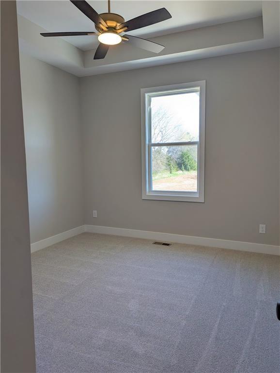 empty room featuring a tray ceiling, light carpet, visible vents, and baseboards