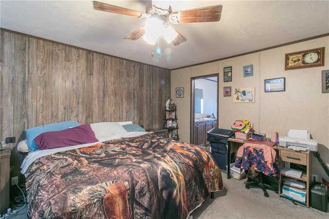 bedroom featuring ceiling fan, light carpet, a textured ceiling, wooden walls, and ensuite bathroom