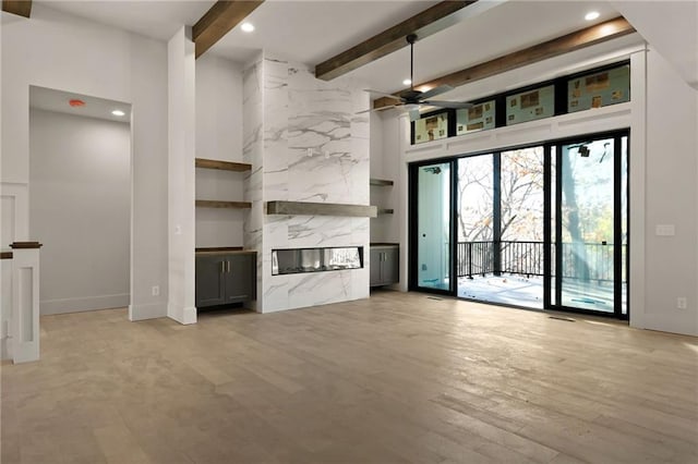 unfurnished living room with beamed ceiling, a premium fireplace, ceiling fan, and light wood-type flooring