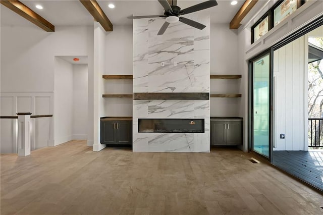 unfurnished living room with a fireplace, a towering ceiling, beamed ceiling, ceiling fan, and light hardwood / wood-style flooring