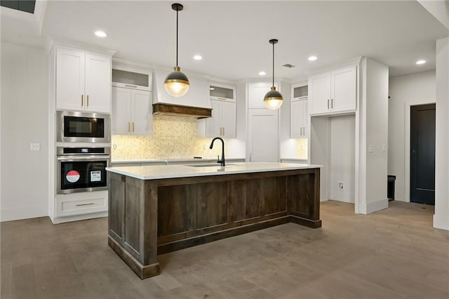 kitchen with sink, appliances with stainless steel finishes, hanging light fixtures, hardwood / wood-style floors, and a kitchen island with sink