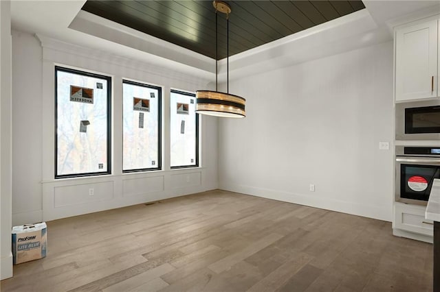 unfurnished dining area featuring light wood-type flooring and a tray ceiling