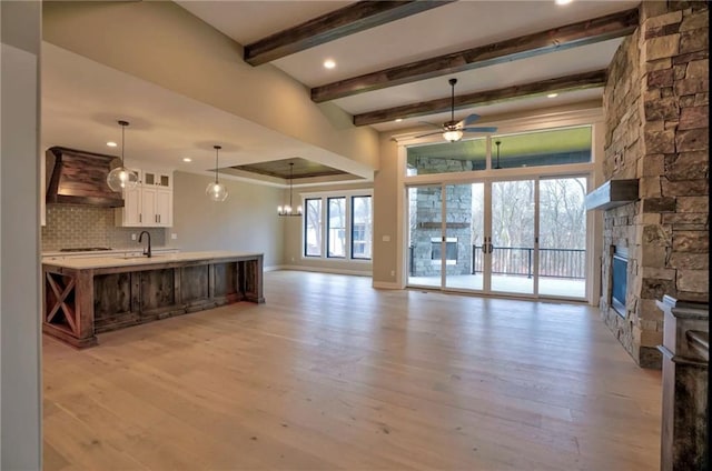 kitchen featuring ceiling fan with notable chandelier, backsplash, a fireplace, light hardwood / wood-style flooring, and premium range hood