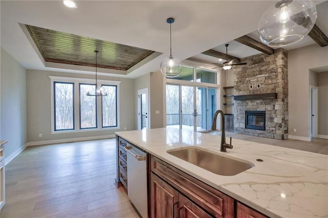 kitchen with a stone fireplace, hanging light fixtures, sink, light stone countertops, and light hardwood / wood-style flooring